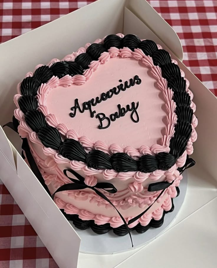 a pink and black heart shaped cake in a box on a checkered tablecloth