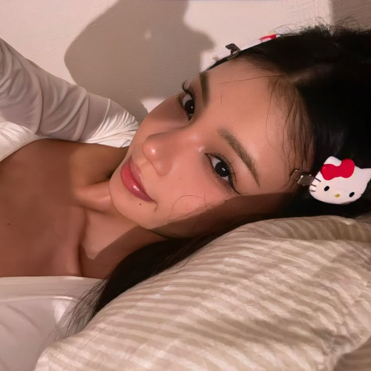 a woman laying on top of a bed next to a white wall with hello kitty hair clips