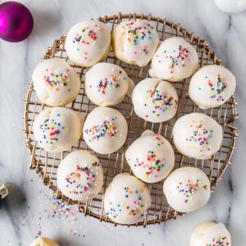 white frosted donuts with sprinkles on a wire rack next to christmas ornaments