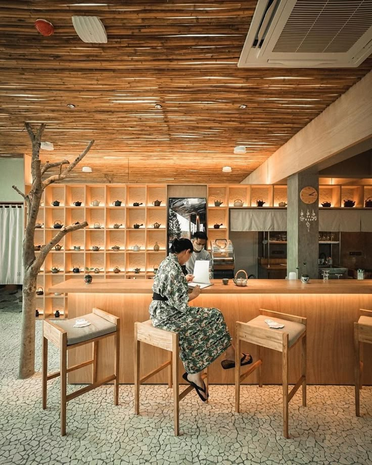 a woman sitting at a counter in a kitchen next to two stools and a tree