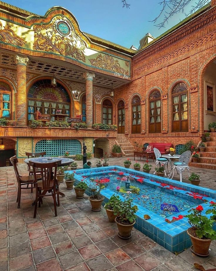 an indoor swimming pool surrounded by potted plants and flowers in front of a red brick building