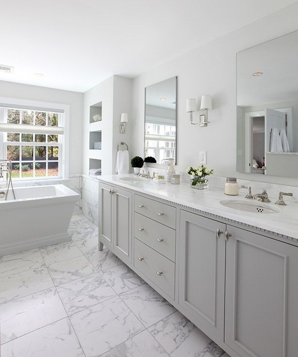 a white bathroom with marble flooring and large tub in the center, surrounded by two windows