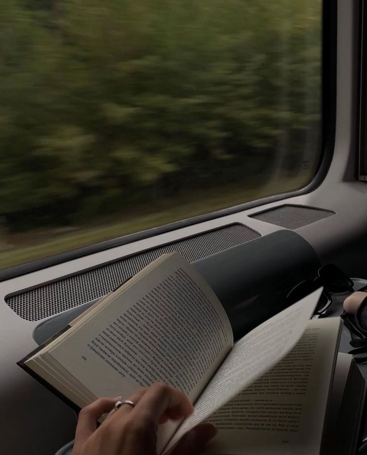 a person is reading a book while riding on a train with trees in the background