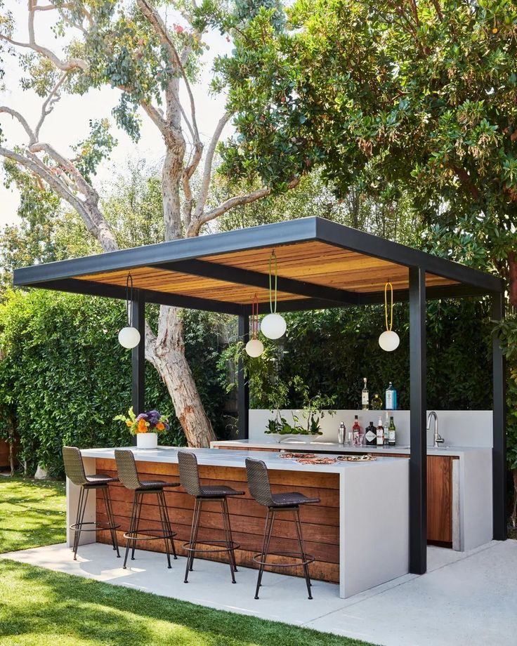 an outdoor bar with stools next to it under a tree and some trees in the background