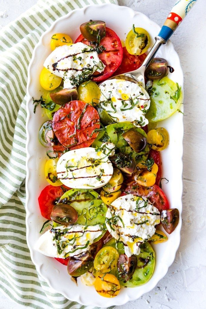 a white platter filled with tomatoes, cucumbers and mozzarella