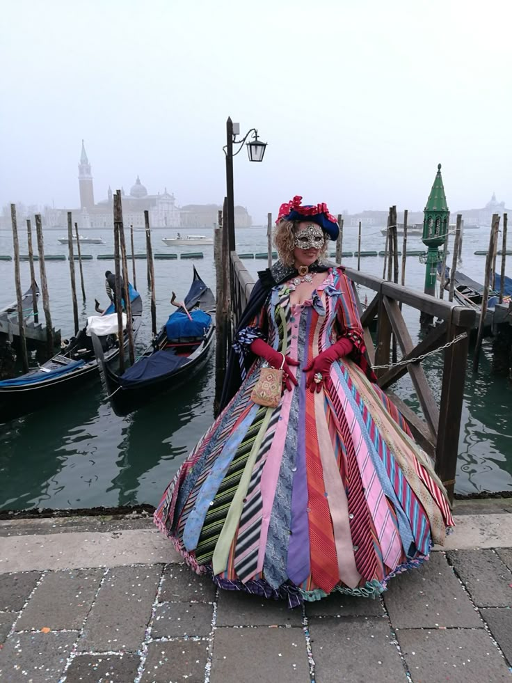 a woman in a colorful dress standing next to a dock with gondolas on the water