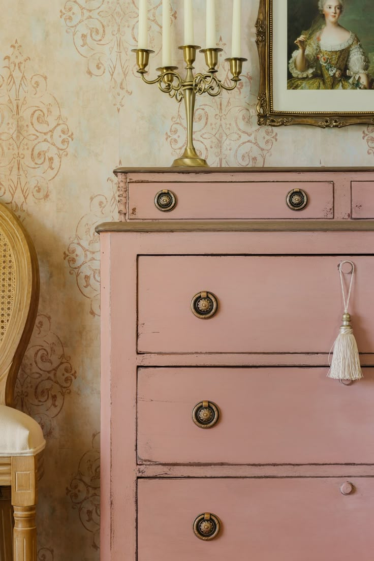 a pink dresser with two candles on top of it and a painting in the background