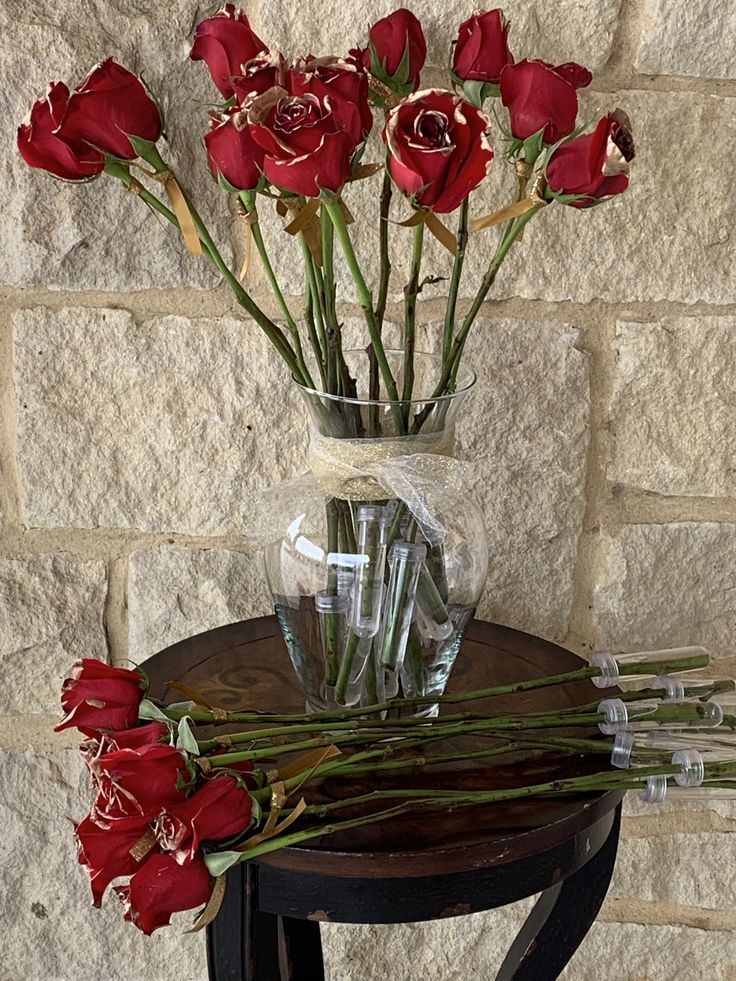 a vase filled with red roses sitting on top of a table next to a brick wall