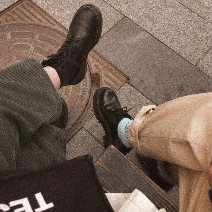 two people sitting on the ground with their feet up and one person wearing black shoes