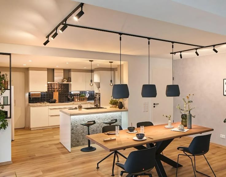 a kitchen and dining room with wood flooring, white walls and ceiling lights hanging from the ceiling