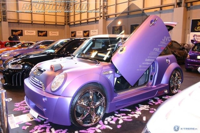 several cars are parked in a showroom with flowers on the floor and one car has its door open