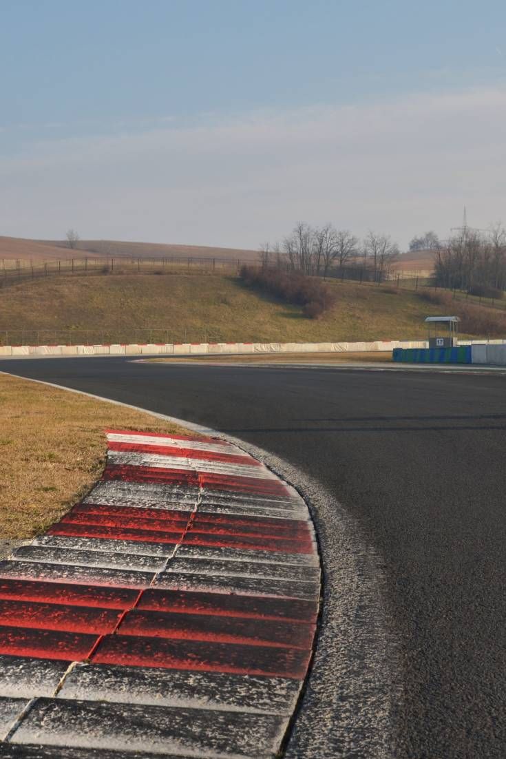 an empty race track with red and white painted lines on it's sides, in the middle of nowhere