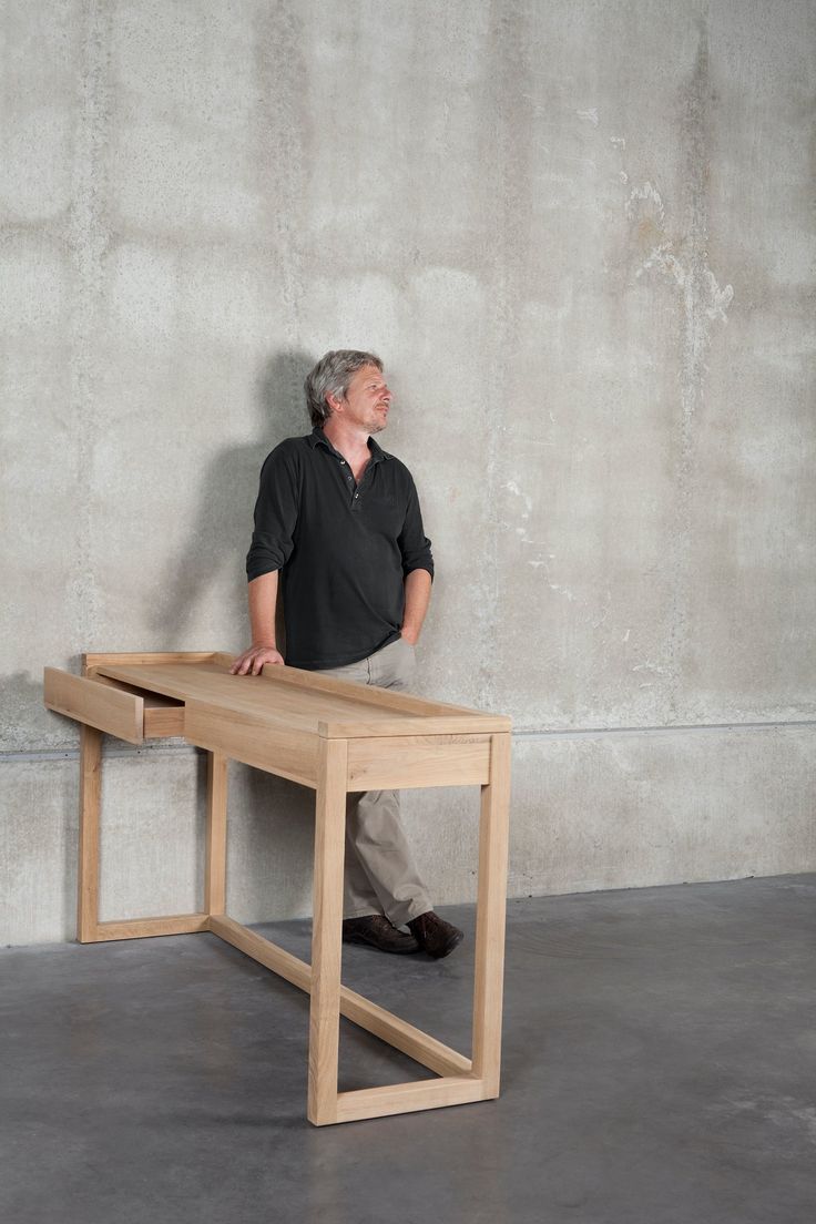 a man standing next to a wooden table in front of a concrete wall with one leg on the ground