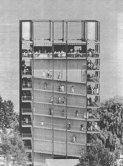 a tall building with people standing on the balconies in front of trees and water