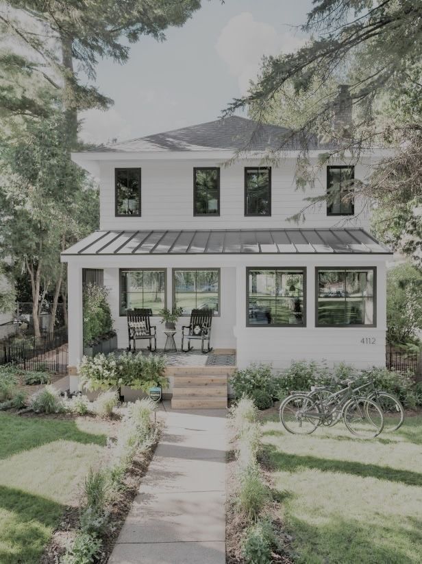 a white house with two bikes parked in front of it and trees around the yard