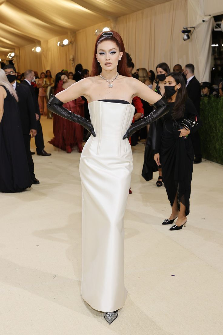 a woman in a white gown and black gloves at the mete galas, with her hands on her hips