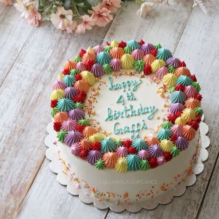 a birthday cake with colorful icing and flowers in the background on a wooden table