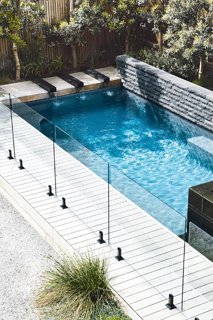 an above ground swimming pool surrounded by plants and trees with water running down the side