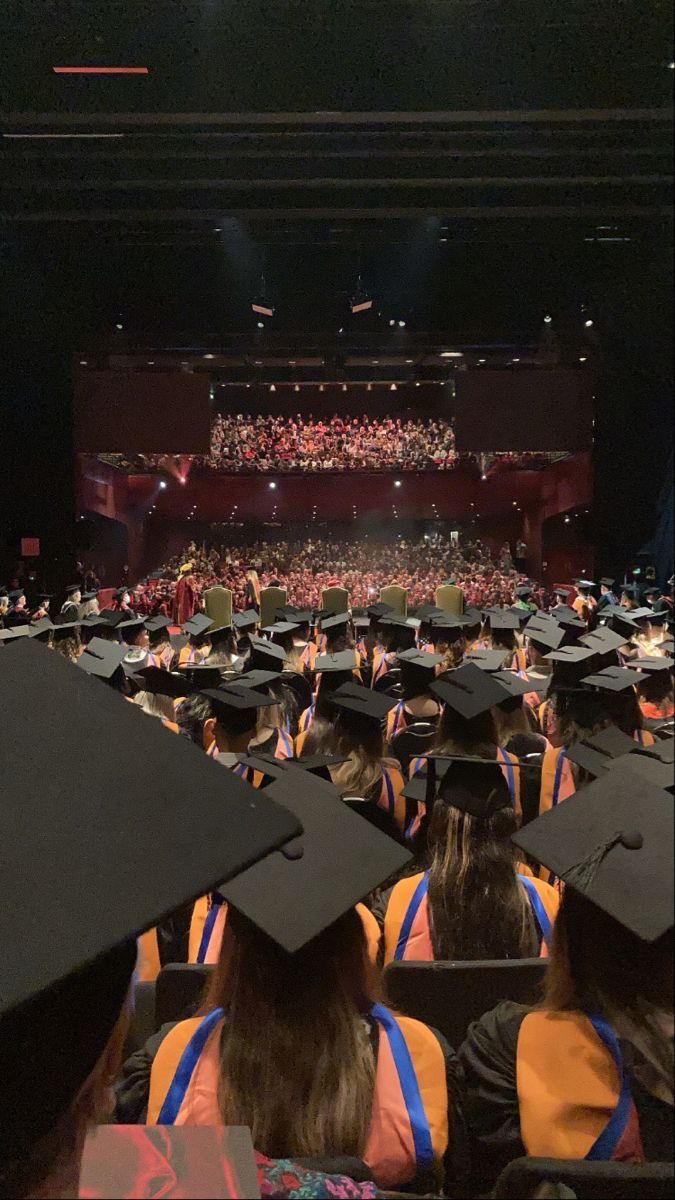 a large group of people in graduation caps and gowns at a stage with an audience