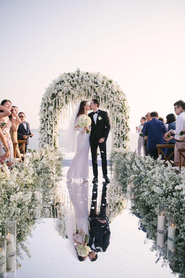 a bride and groom are standing in front of an archway with white flowers on it