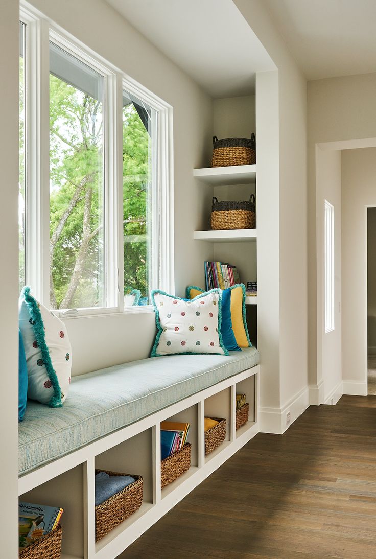 a window seat in the corner of a room with bookshelves and baskets on it