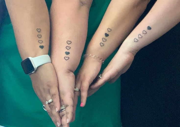 three women with matching tattoos on their arms holding each other's hands in the shape of hearts