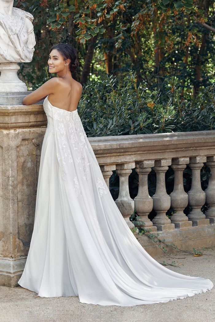 a woman standing next to a statue wearing a white wedding dress with an open back