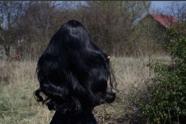 the back of a woman's head with long black hair standing in a field