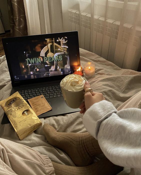 a person sitting on a bed with a cup of coffee in front of a laptop