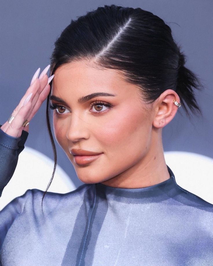 a close up of a person wearing a silver top and holding her hair in the air