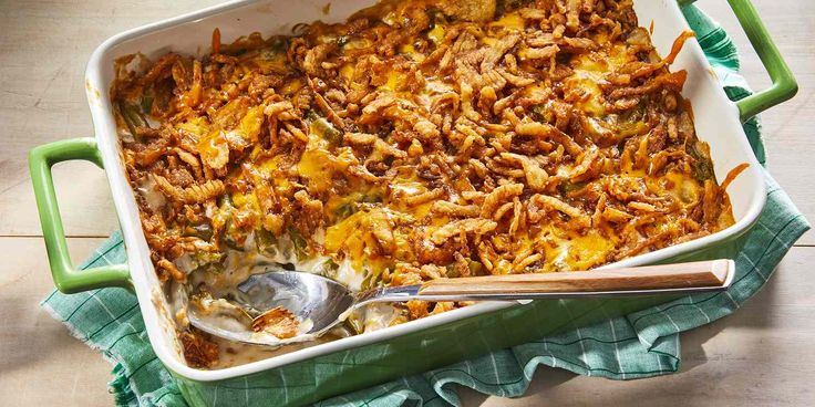 a casserole dish with meat and cheese in it on a green cloth next to a wooden spoon