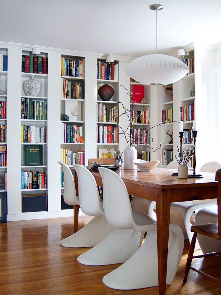 a dining room table with white chairs and bookshelves in the wall behind it