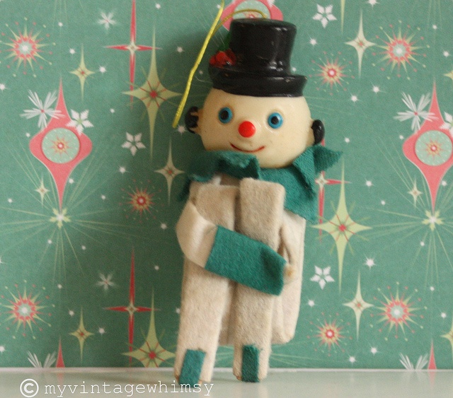 a small toy with a top hat and scarf on it's head is standing in front of a wall