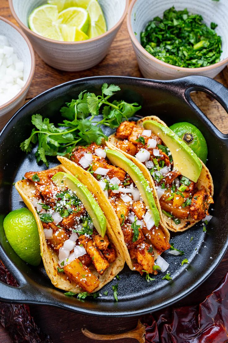 three fish tacos in a skillet with limes and cilantro on the side