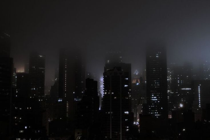 the city skyline is lit up at night with fog and smoggy skies in the background