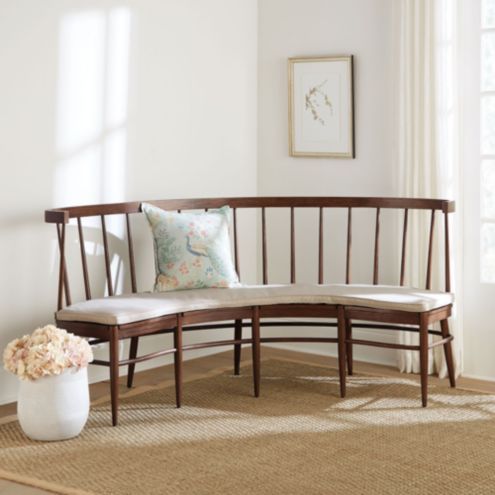 a wooden bench sitting on top of a rug next to a vase filled with flowers