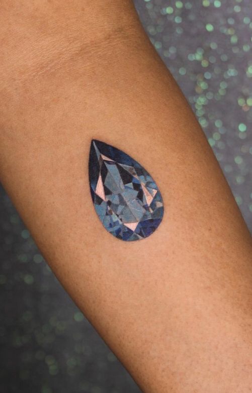 a woman's arm with a blue diamond tattoo on it