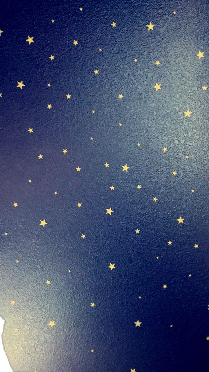 a teddy bear sitting on top of a bed next to a night sky wallpaper