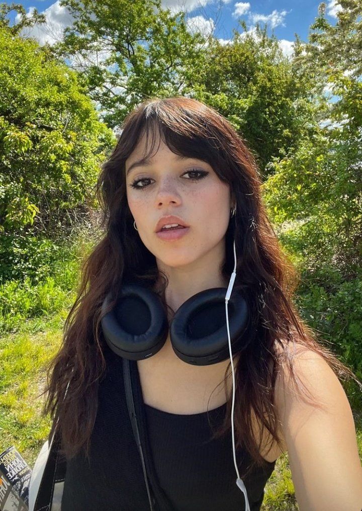 a woman wearing headphones standing in front of trees