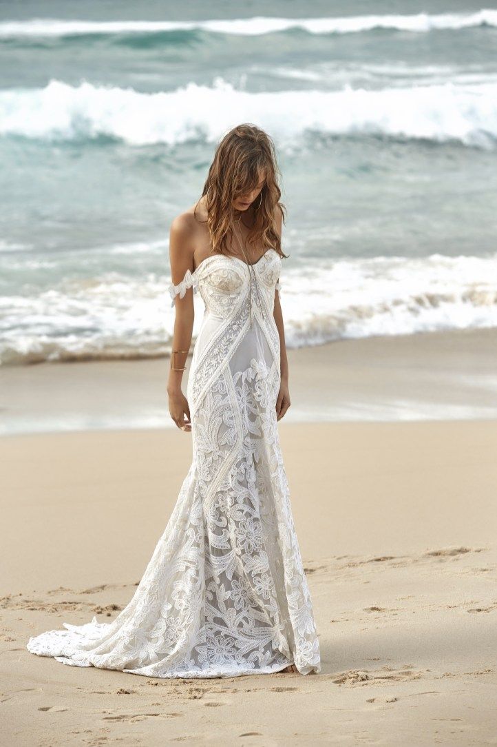 a woman standing on top of a sandy beach next to the ocean in a white dress