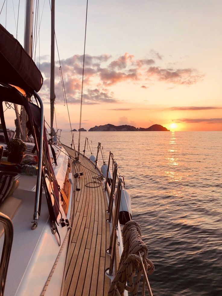 the sun is setting over the ocean on a sailboat