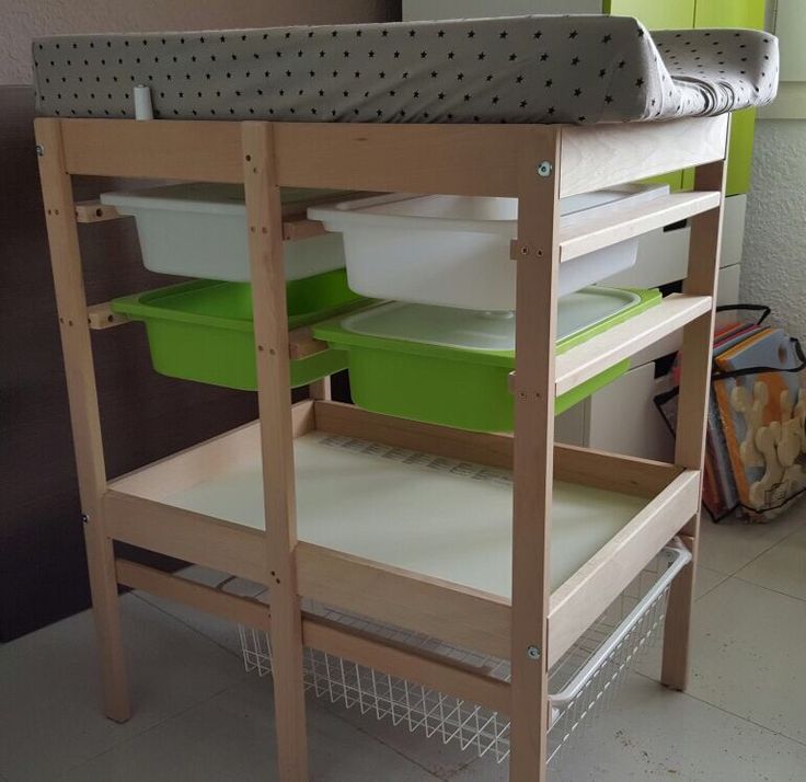 a baby changing table with green and white containers on it's bottom shelf next to a wall