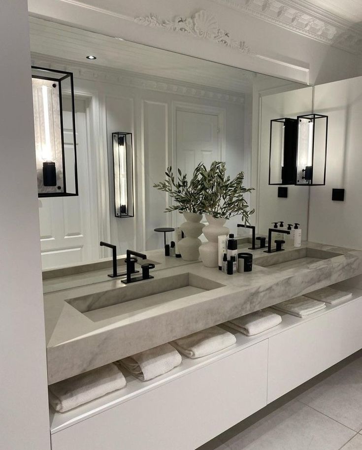 a bathroom with double sinks and mirrors in the wall, along with two vases filled with flowers