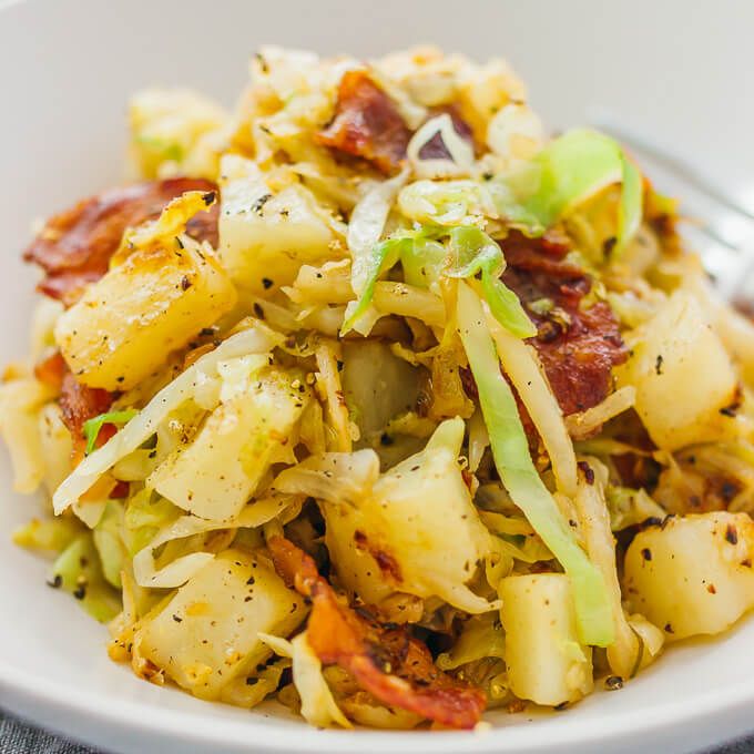 a white bowl filled with pasta and bacon on top of a table next to a fork