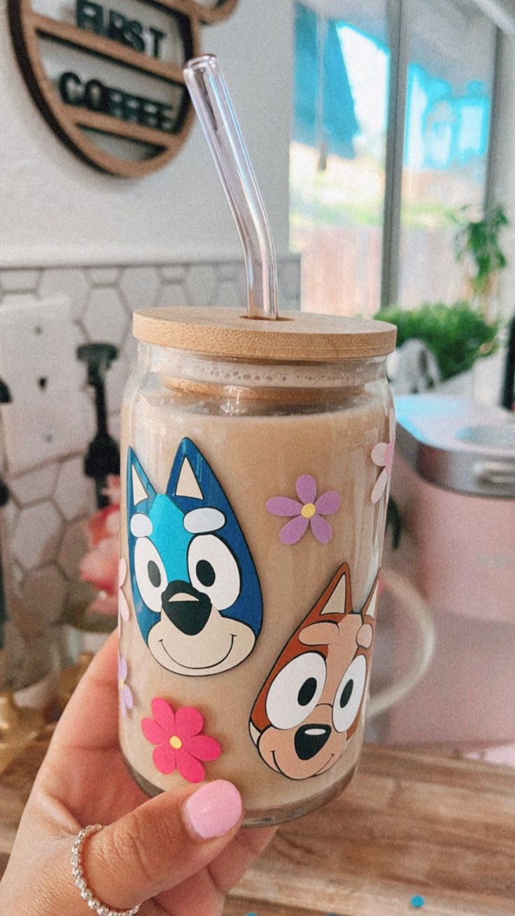 a hand holding a glass with cartoon characters on it and a straw in the cup