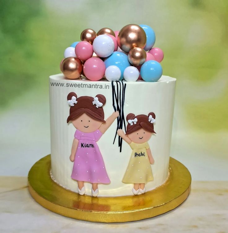 there is a cake with two girls on it and balloons in the air above them