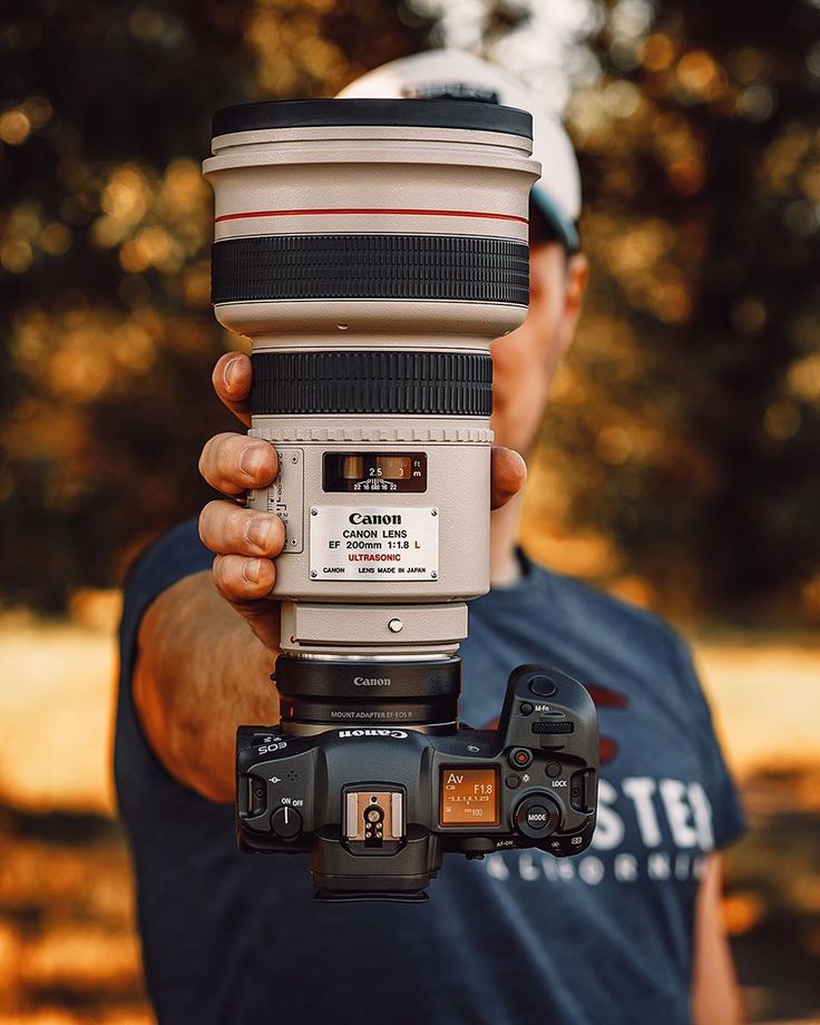 a man holding up a camera with a lens attached to it's body in front of trees