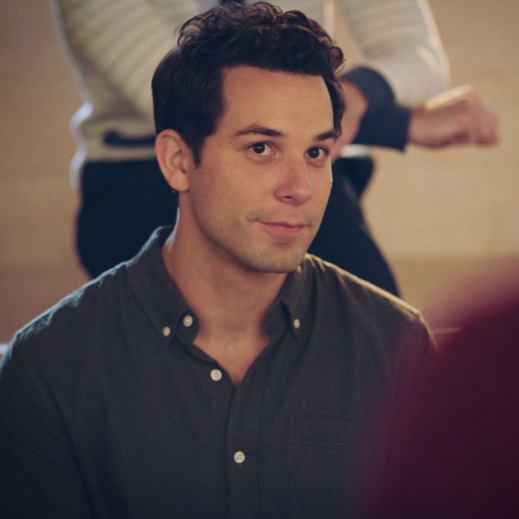 a man in a black shirt is looking at the camera while another person sits behind him