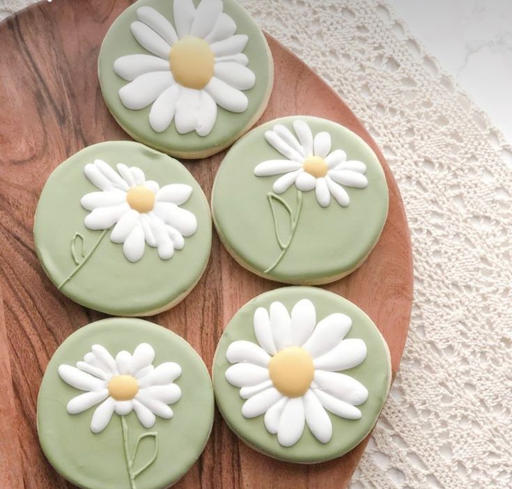 four cookies decorated with green icing and white daisies on a wooden platter