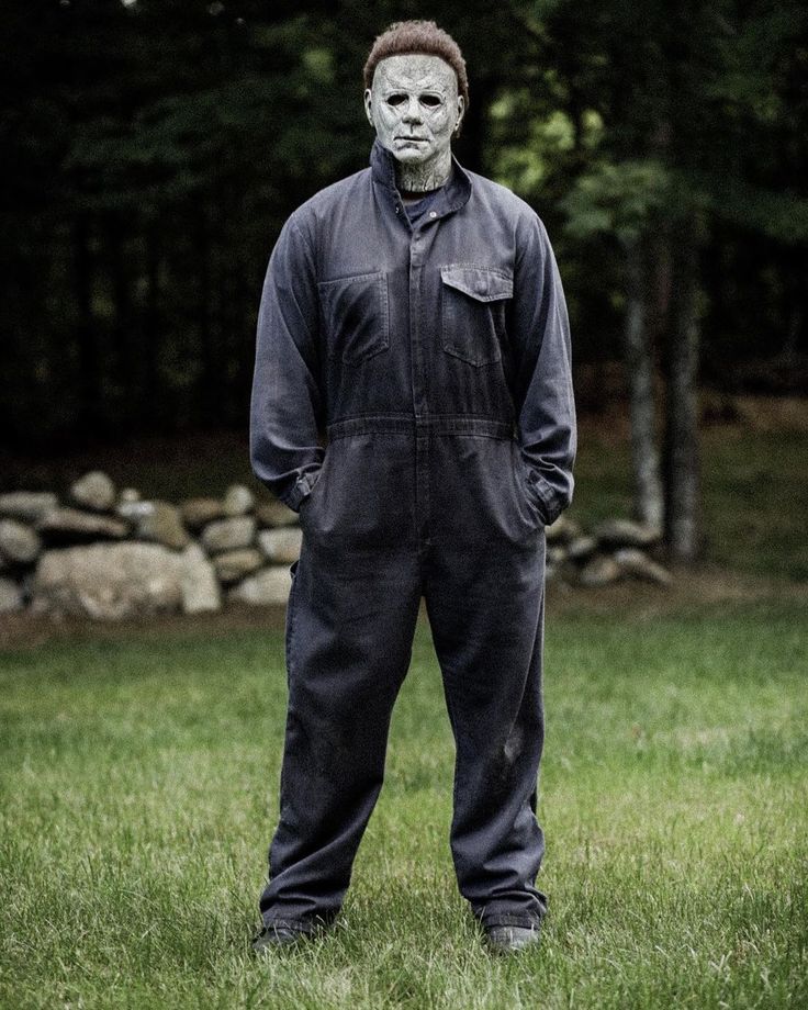 a man wearing a mask and overalls standing in the grass with his hands on his hips